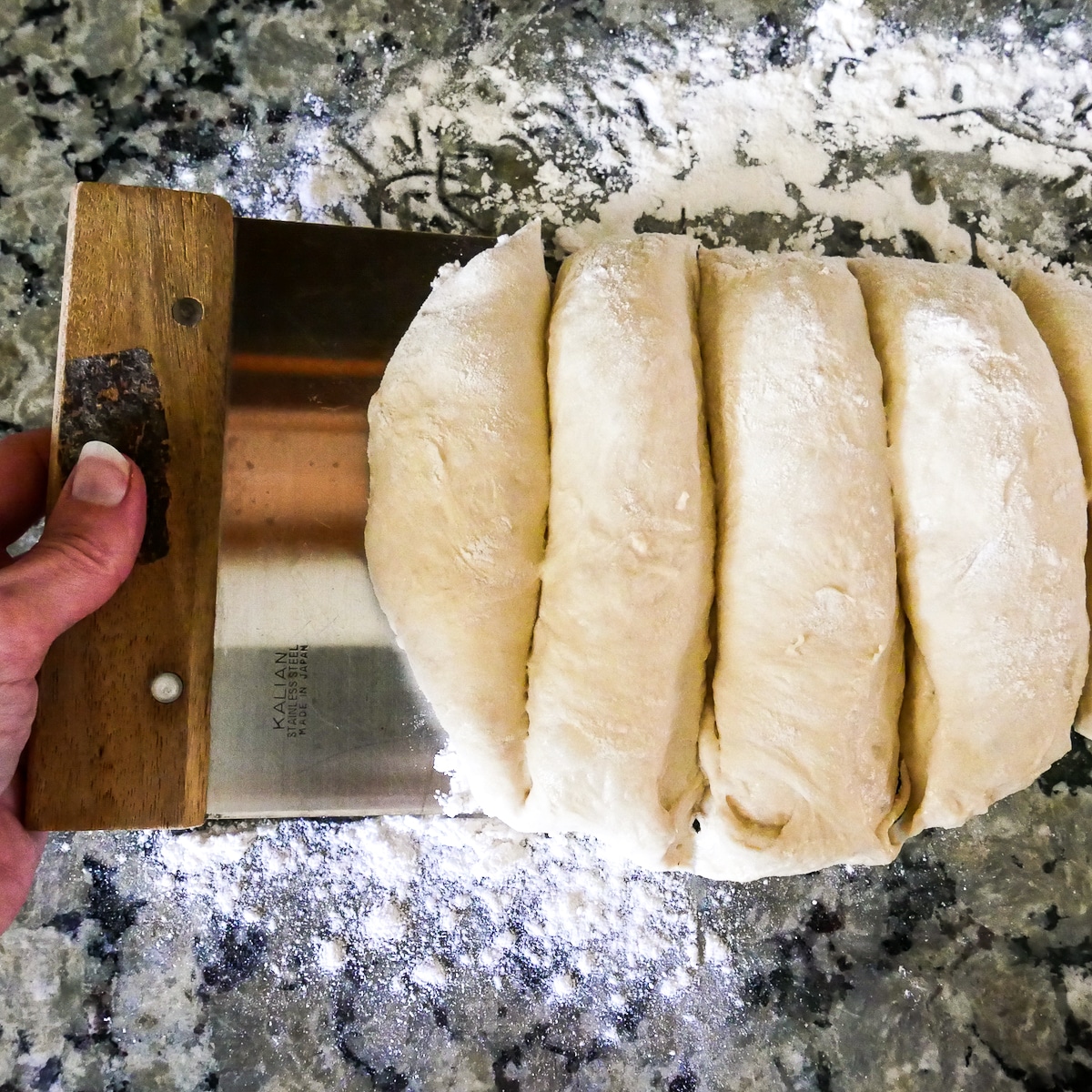 Ciabatta rolls divided into 4 parts with a bench scraper.