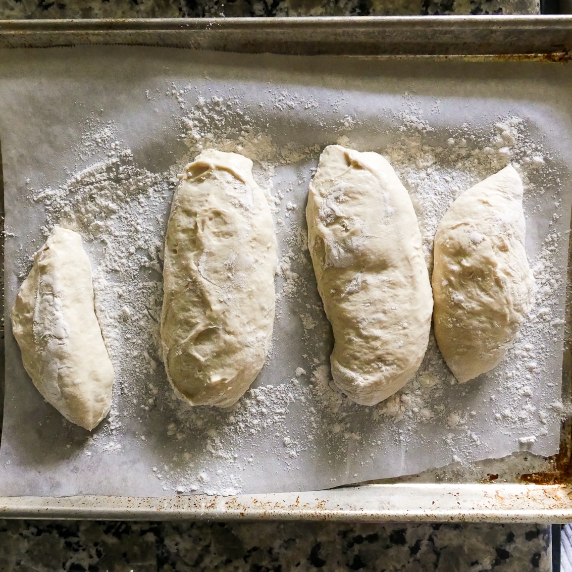 four ciabatta rolls resting on a baking sheet and ready to be baked. 