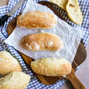 three ciabatta rolls on a wooden cutting board with napkin.