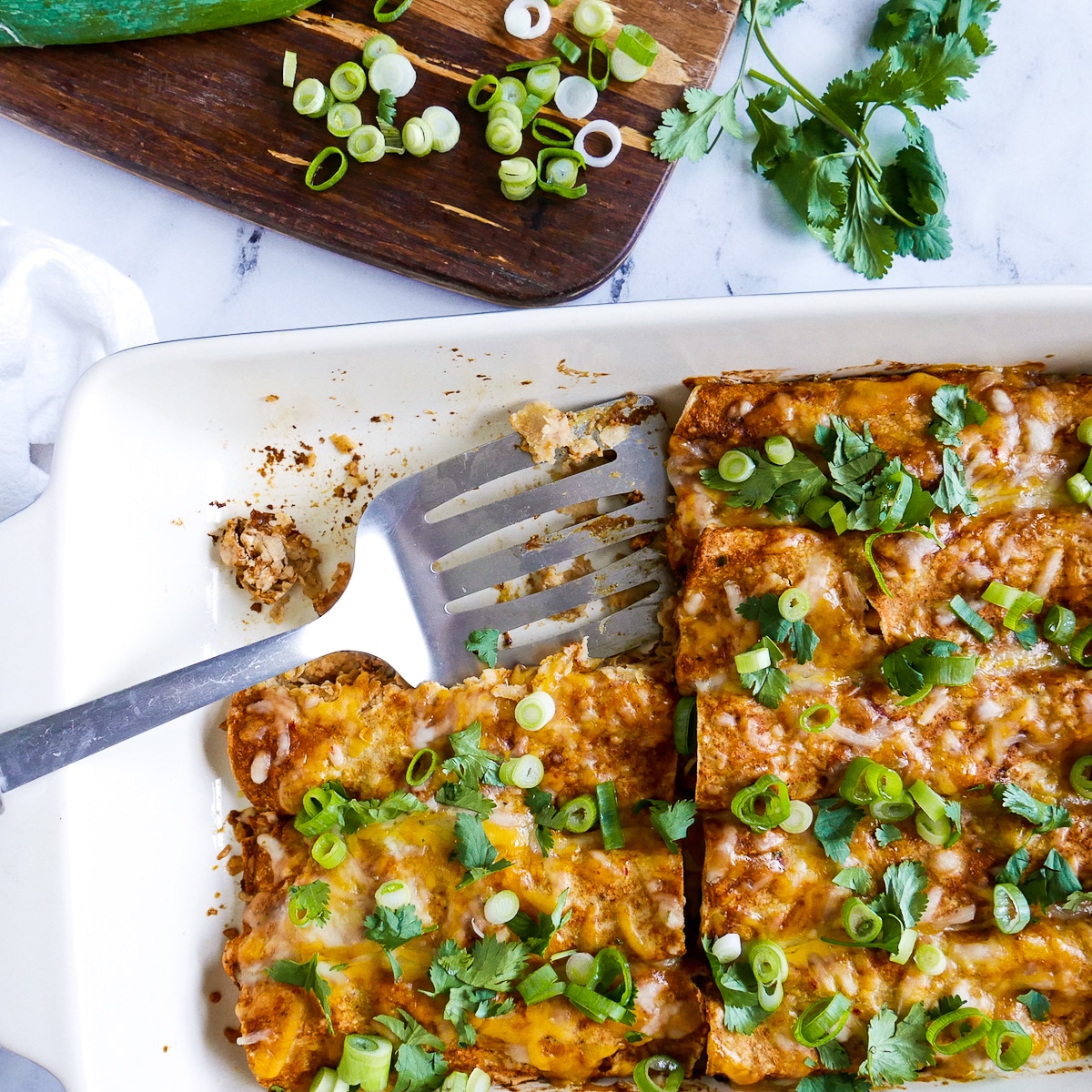 Spatula resting in a pan of enchiladas garnished with scallions and cilantro.