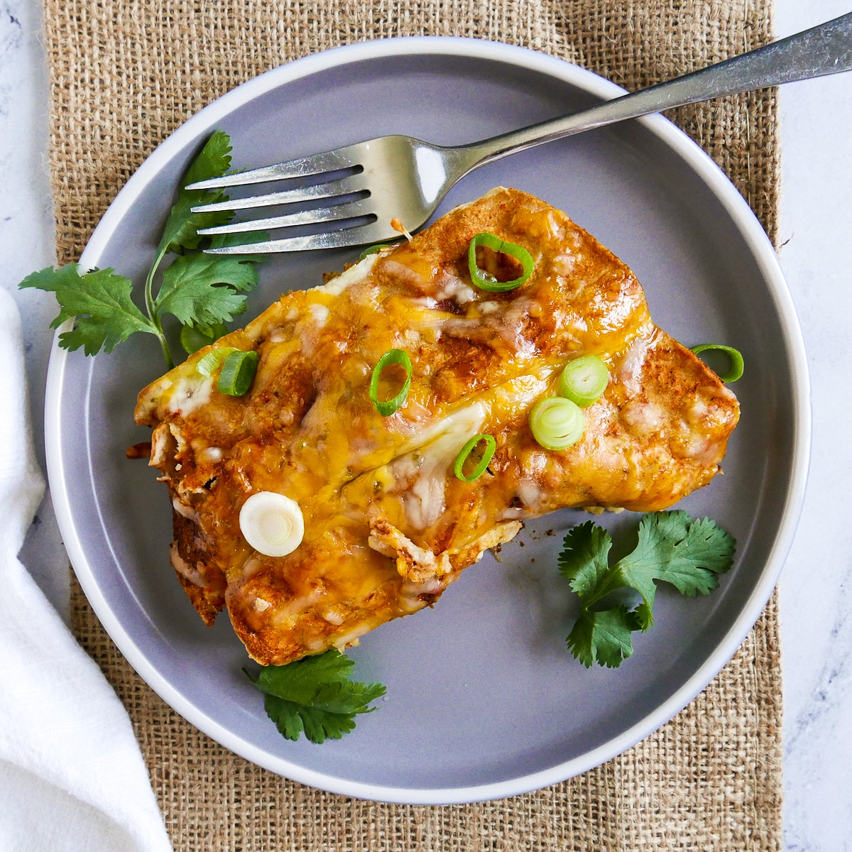 fork resting on gray plate holding two enchiladas.