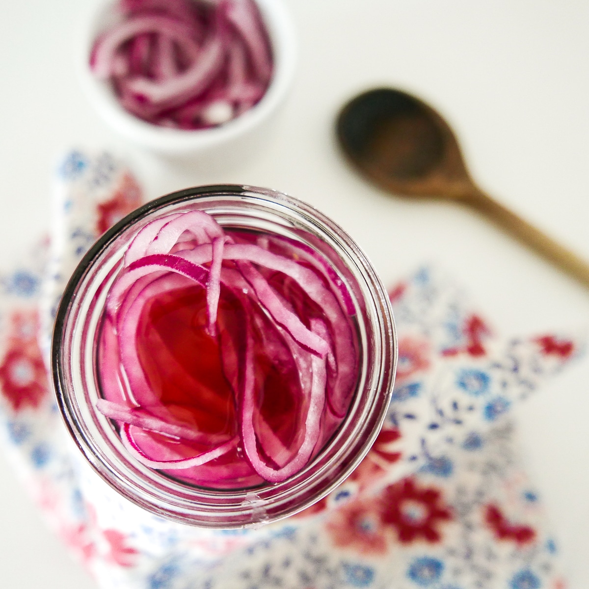 pickled red onions in a jar with wooden spoon in background.