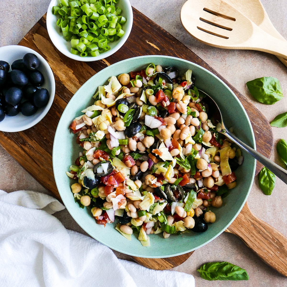 tuscan-bean-salad-with-spoon-and-napkin.jpg bean salad in a bowl with a spoon and resting on a wooden cutting board.