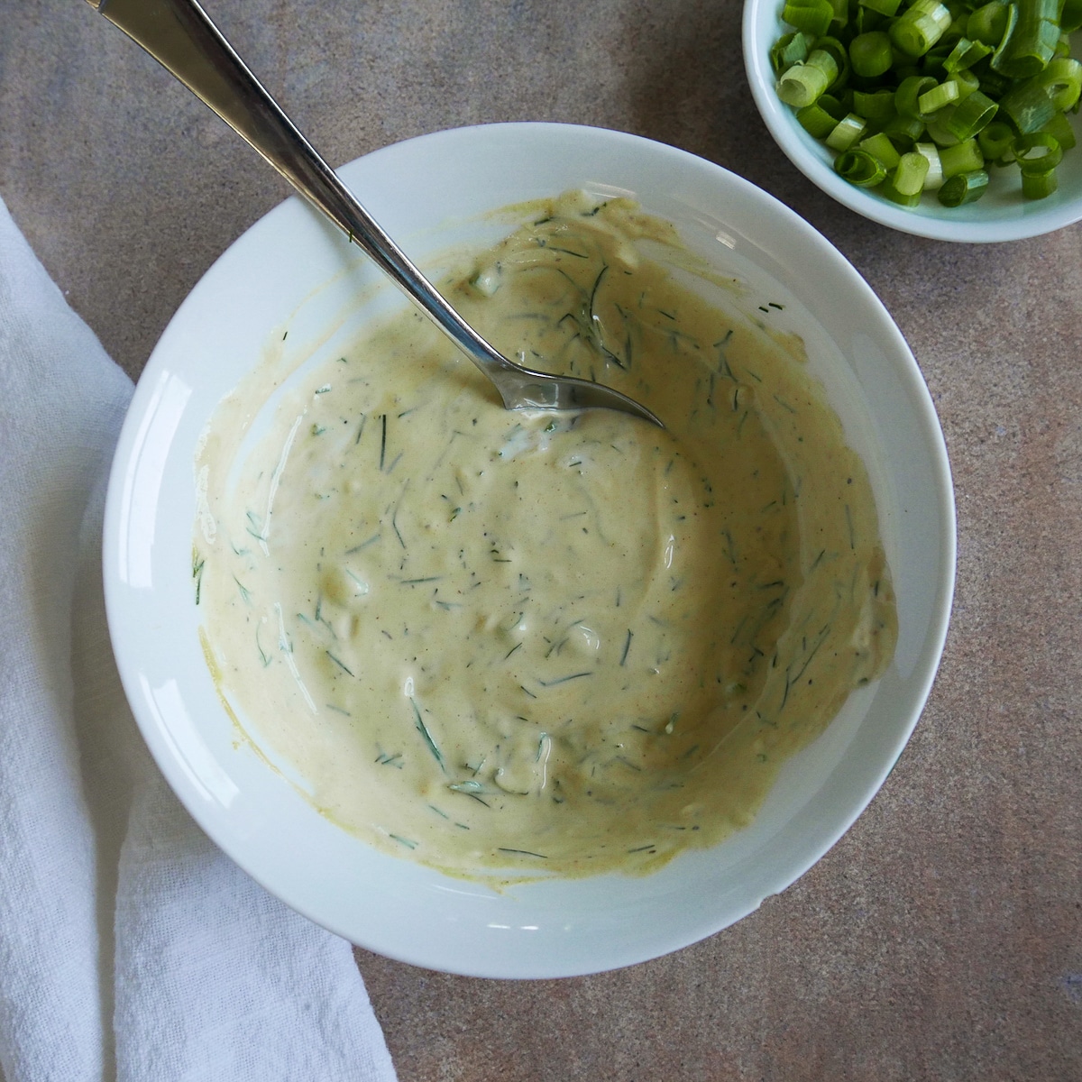 Mustard dill sauce being mixed with a spoon in a small white bowl.