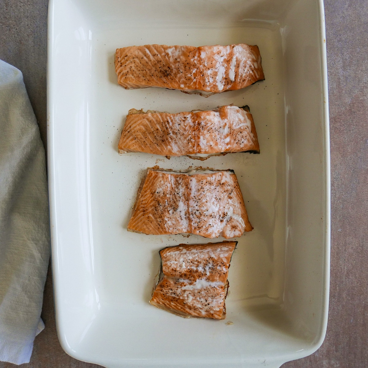 four baked pieces of salmon in a large baking dish.