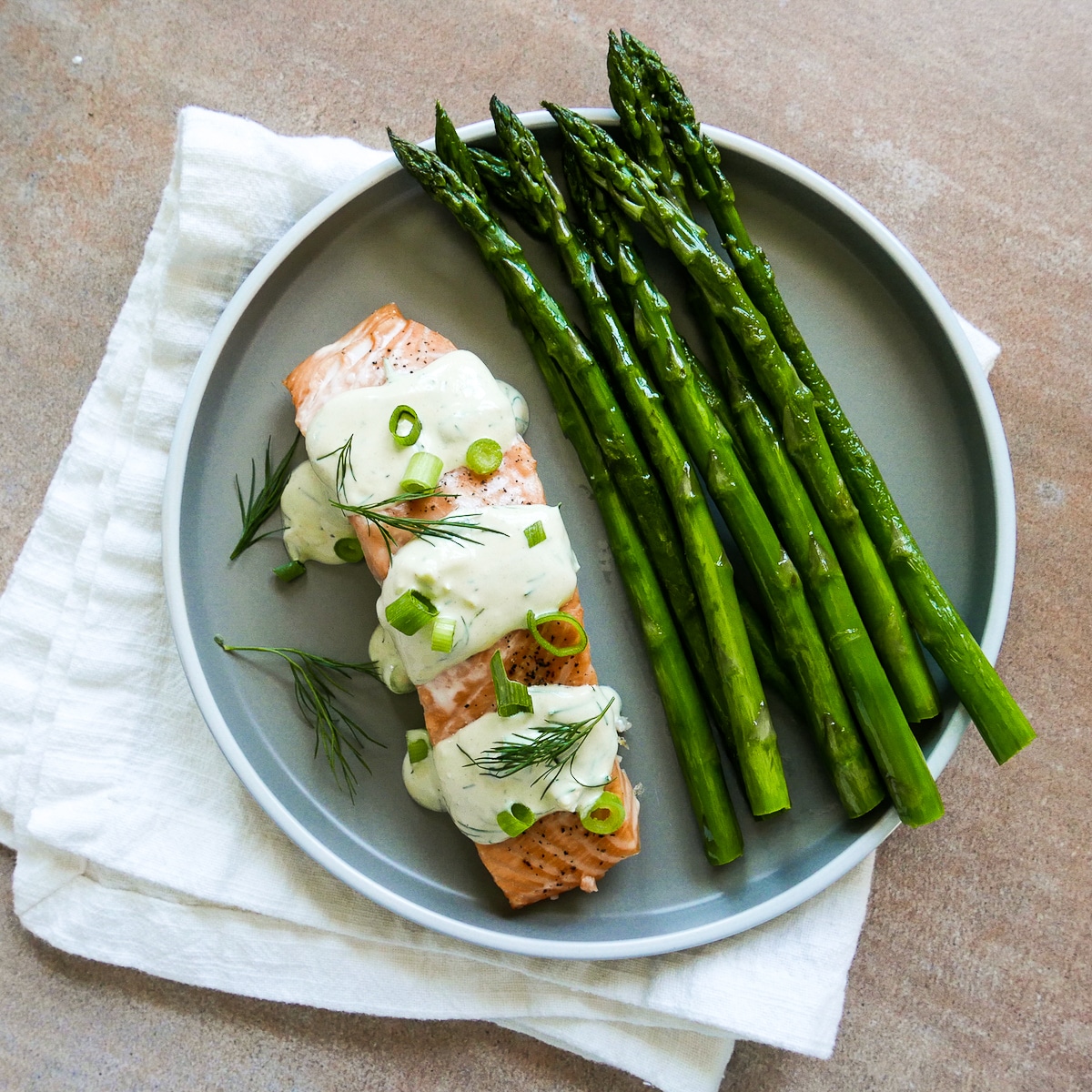 Plate of salmon with dill sauce and roasted asparagus resting on a napkin.