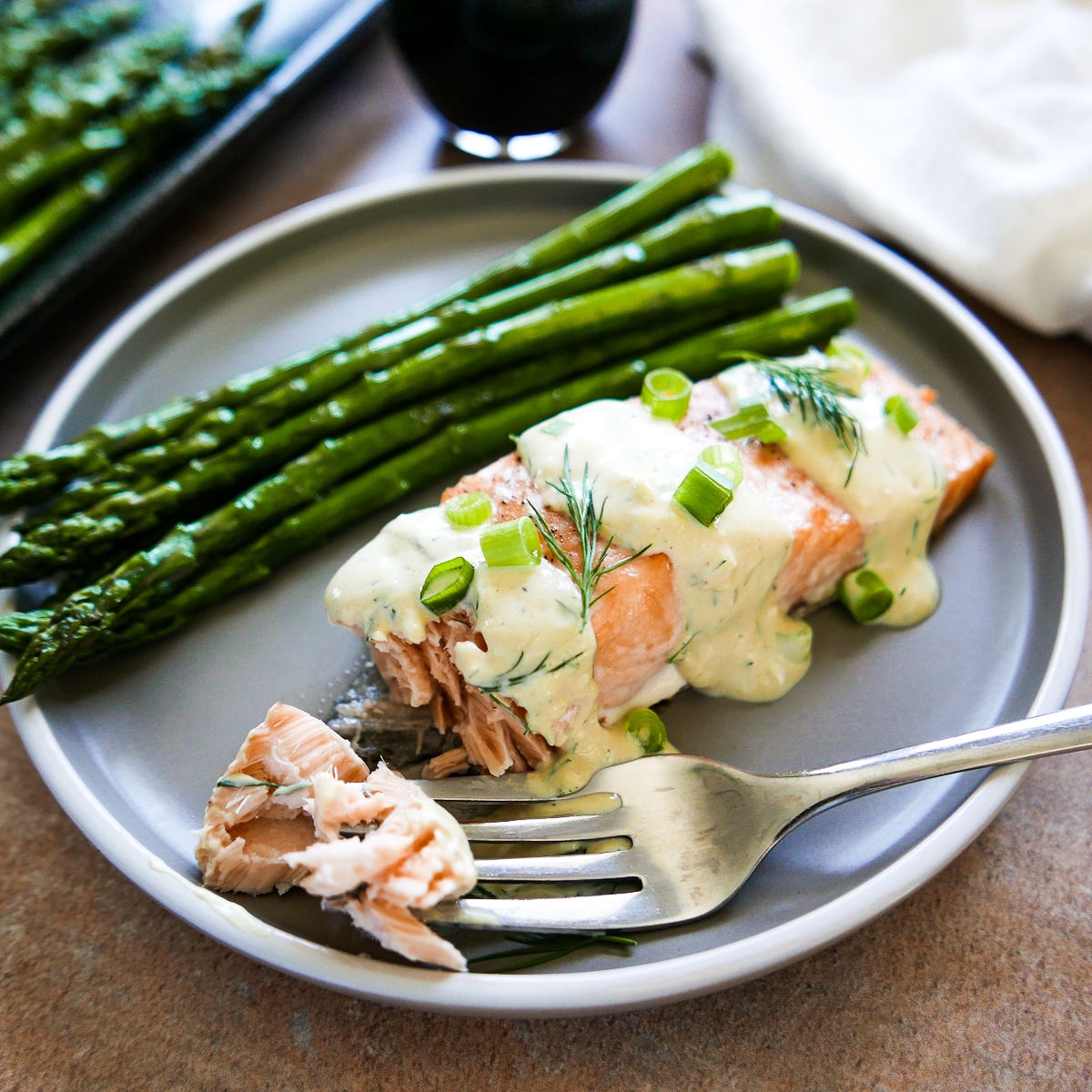 fork holding piece of salmon on plate with salmon and roasted asparagus.