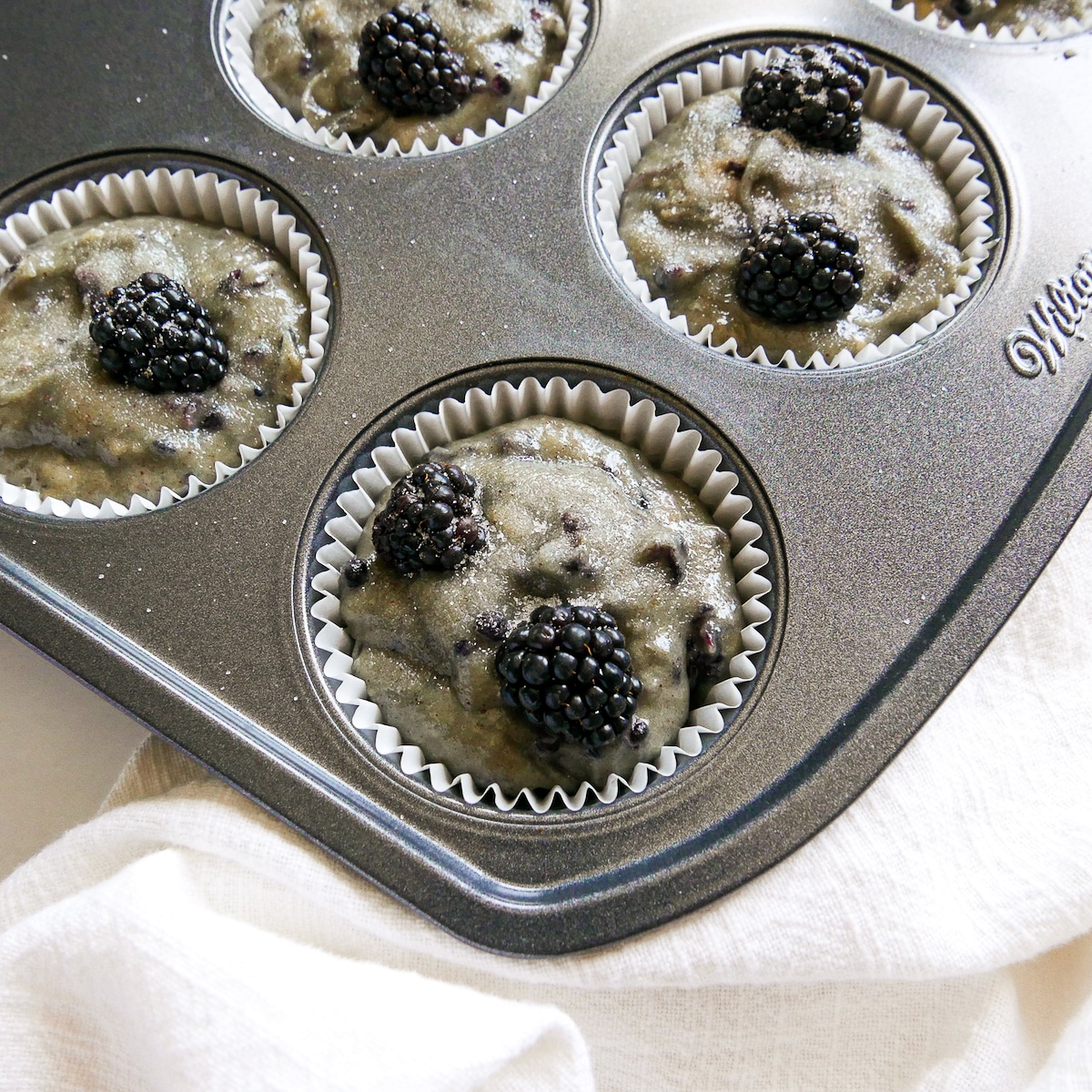 muffin batter in tin with fresh blackberries.