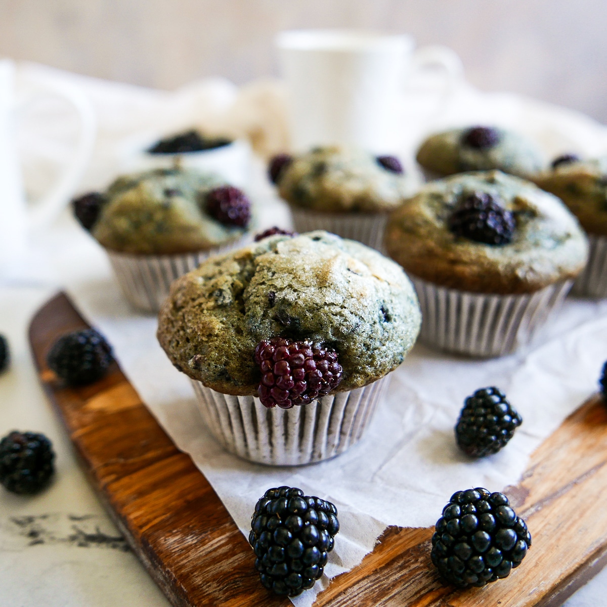 Blackberry muffins arranged on  parchment paper with blackberries scattered around.
