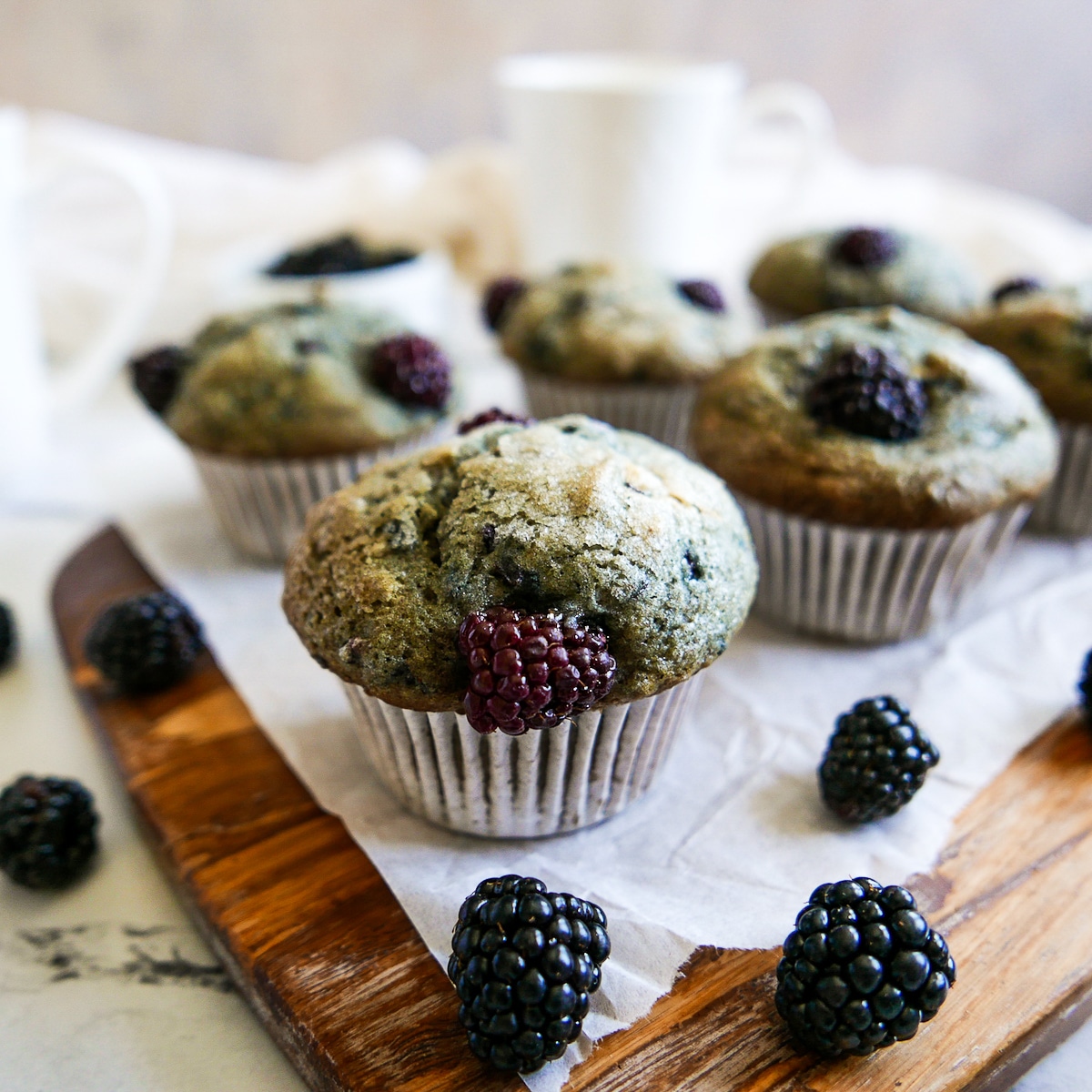 gluten-free-blackberry-muffins.jpg Blackberry muffins arranged on parchment paper with blackberries scattered around.