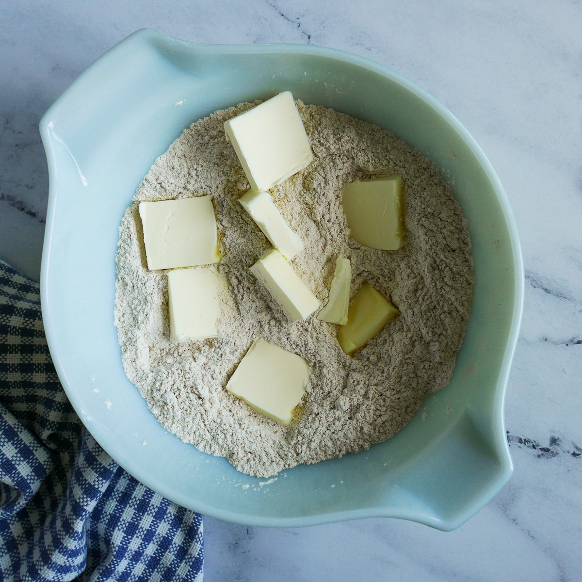 cubes of unsalted butter placed into a bowl of flour. 