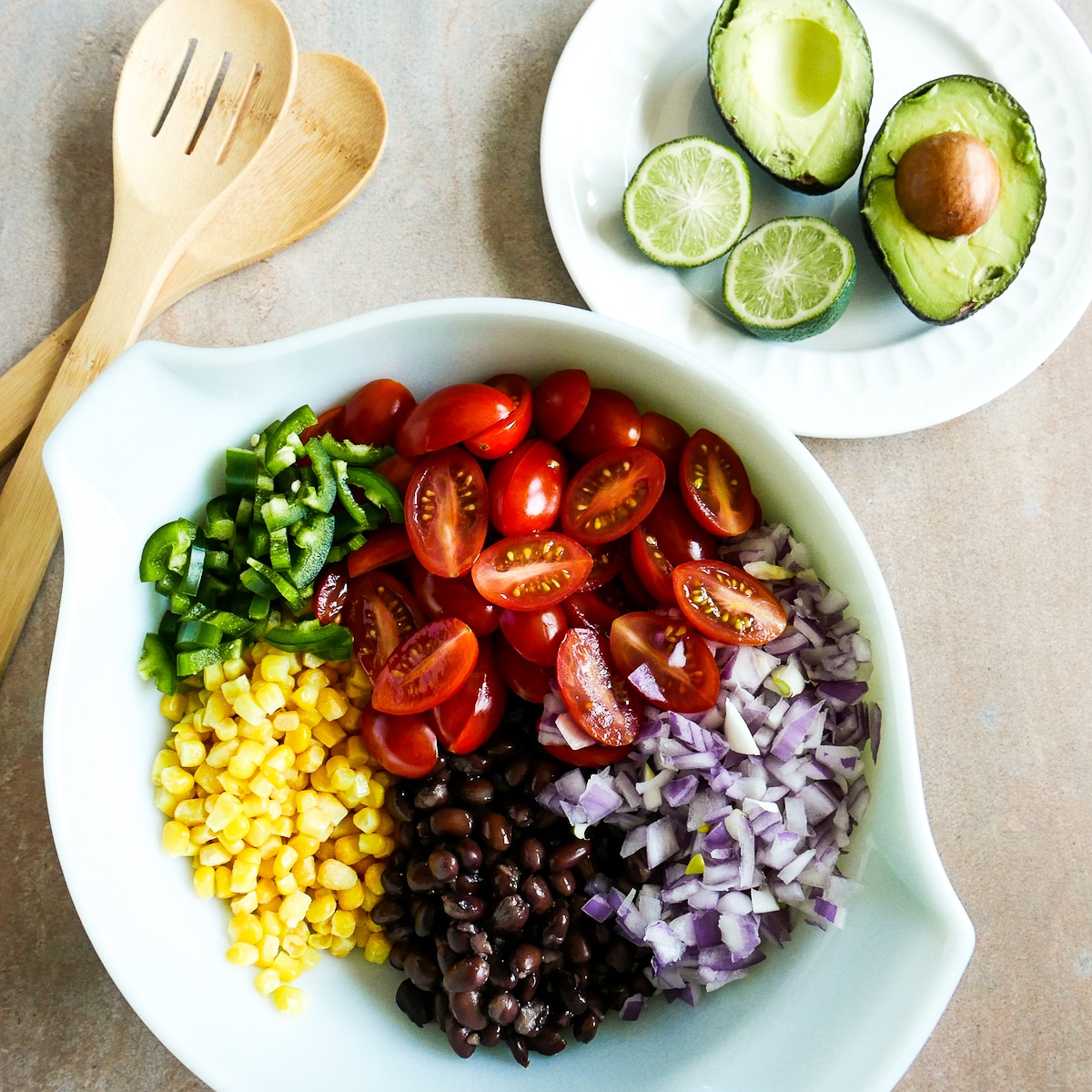 salsa ingredients in a mixing bowl with avocado and cut limes on the side.