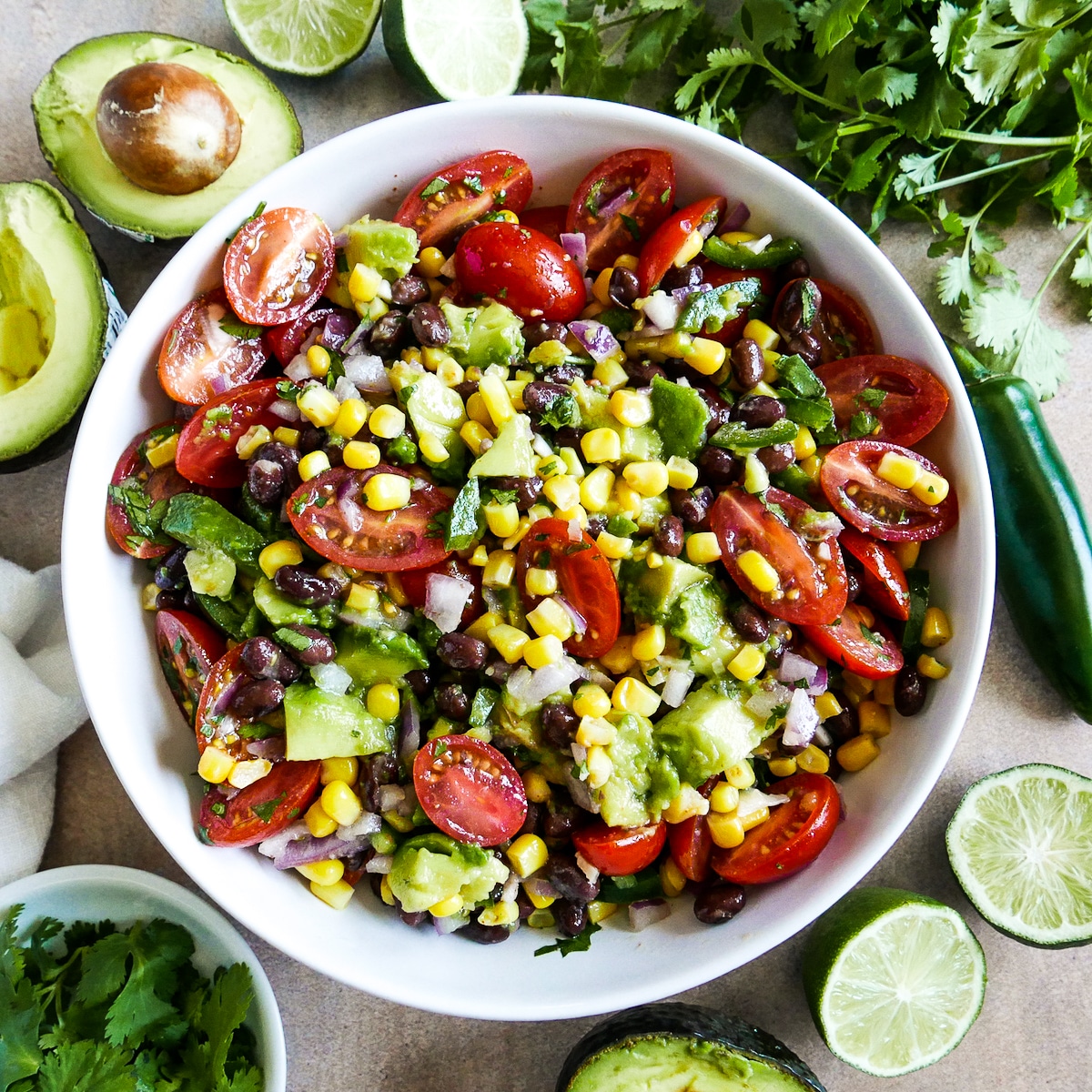 large bowl of salsa arranged with limes, avocado, and cilantro.