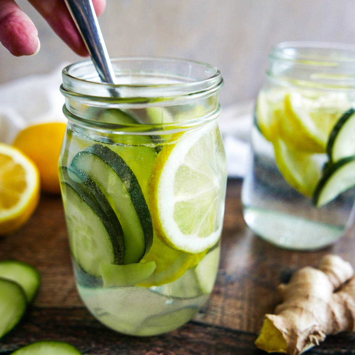 spoon stirring jar of water with sliced lemons and cucumber. 