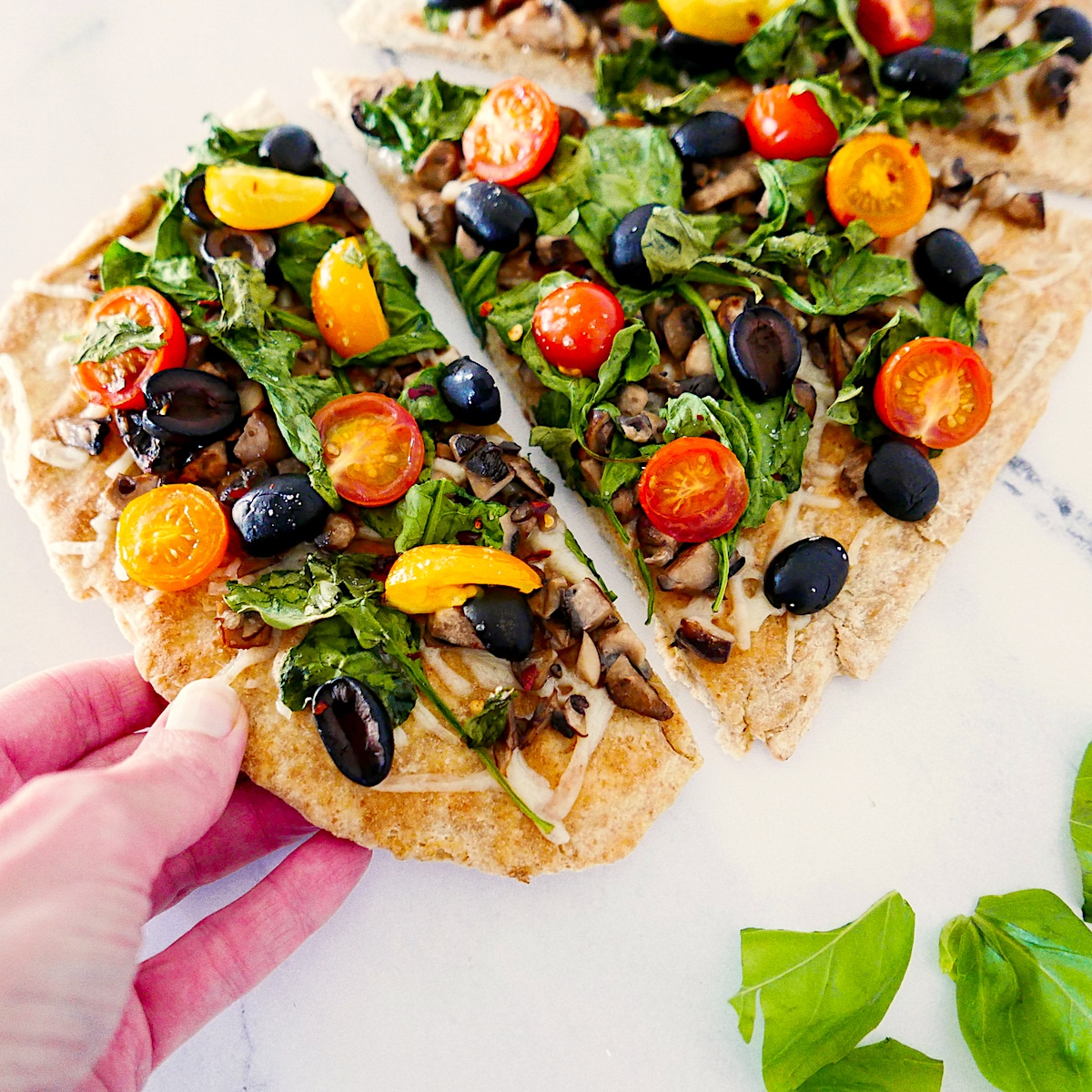 white hand picking up slice of flatbread pizza from table.