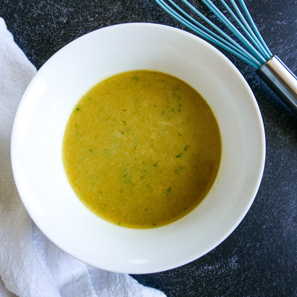 miso dressing in a small white bowl with a whisk resting next to it. 