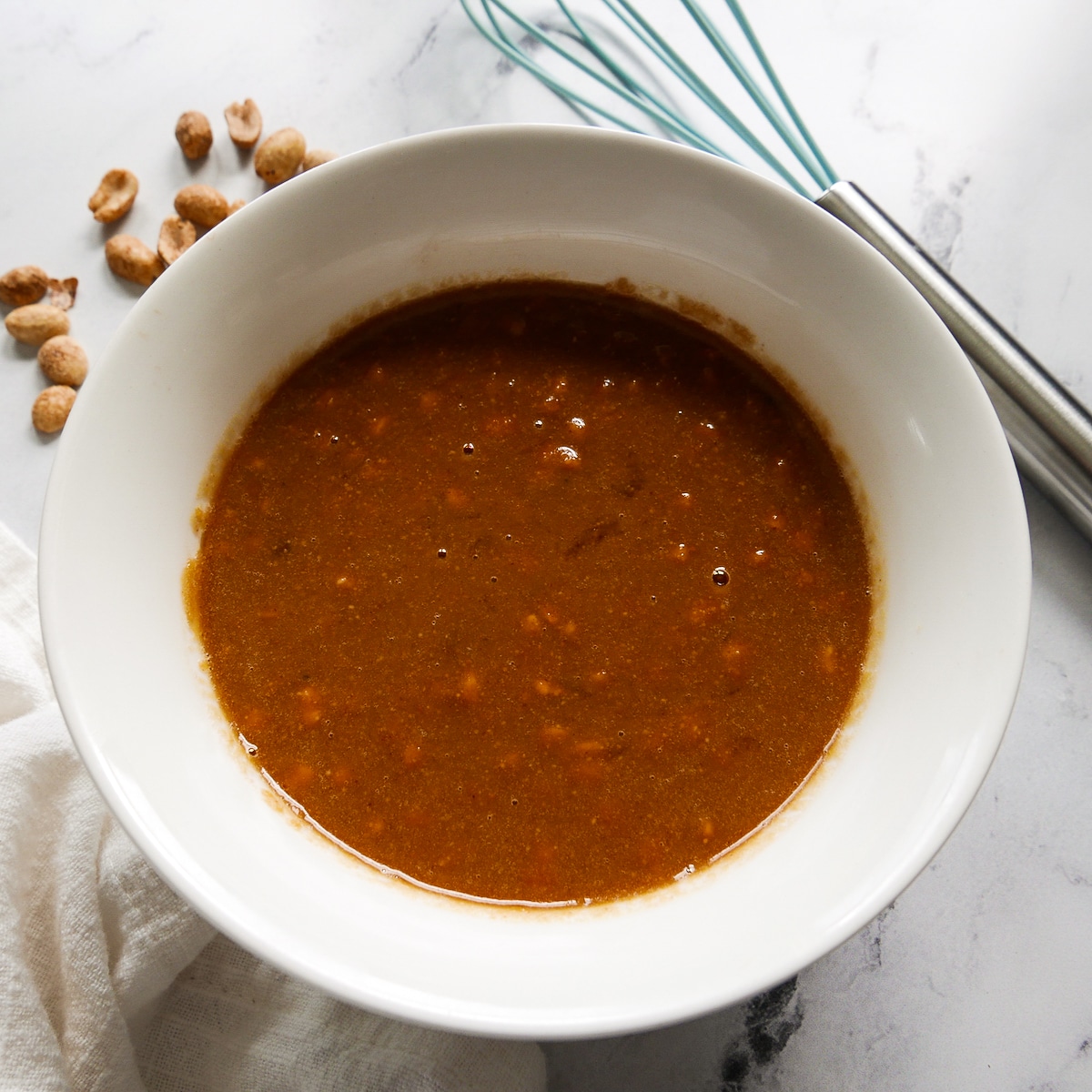 Peanut sauce in a small white bowl with a whisk behind it.