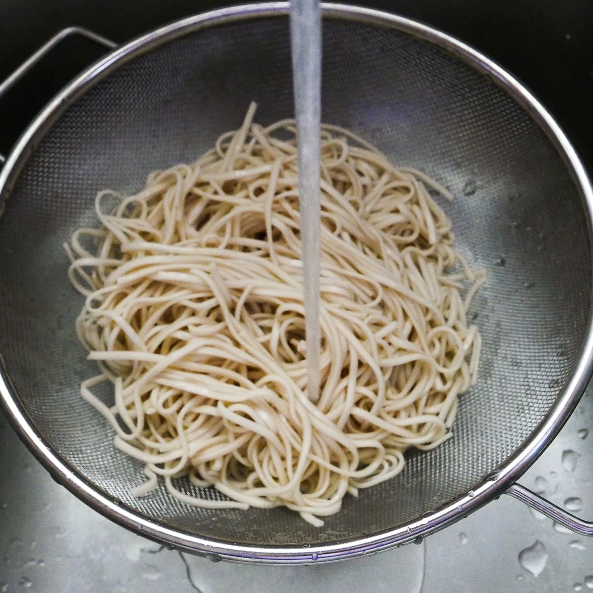 Cooked noodles being rinsed with water in a colander.