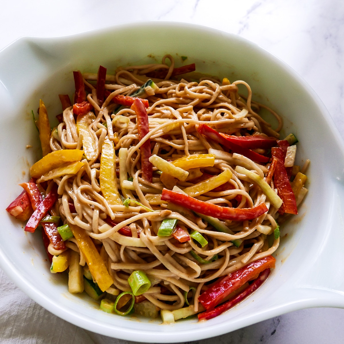 Noodles in a large bowl mixed with peanut sauce and chopped vegetables.