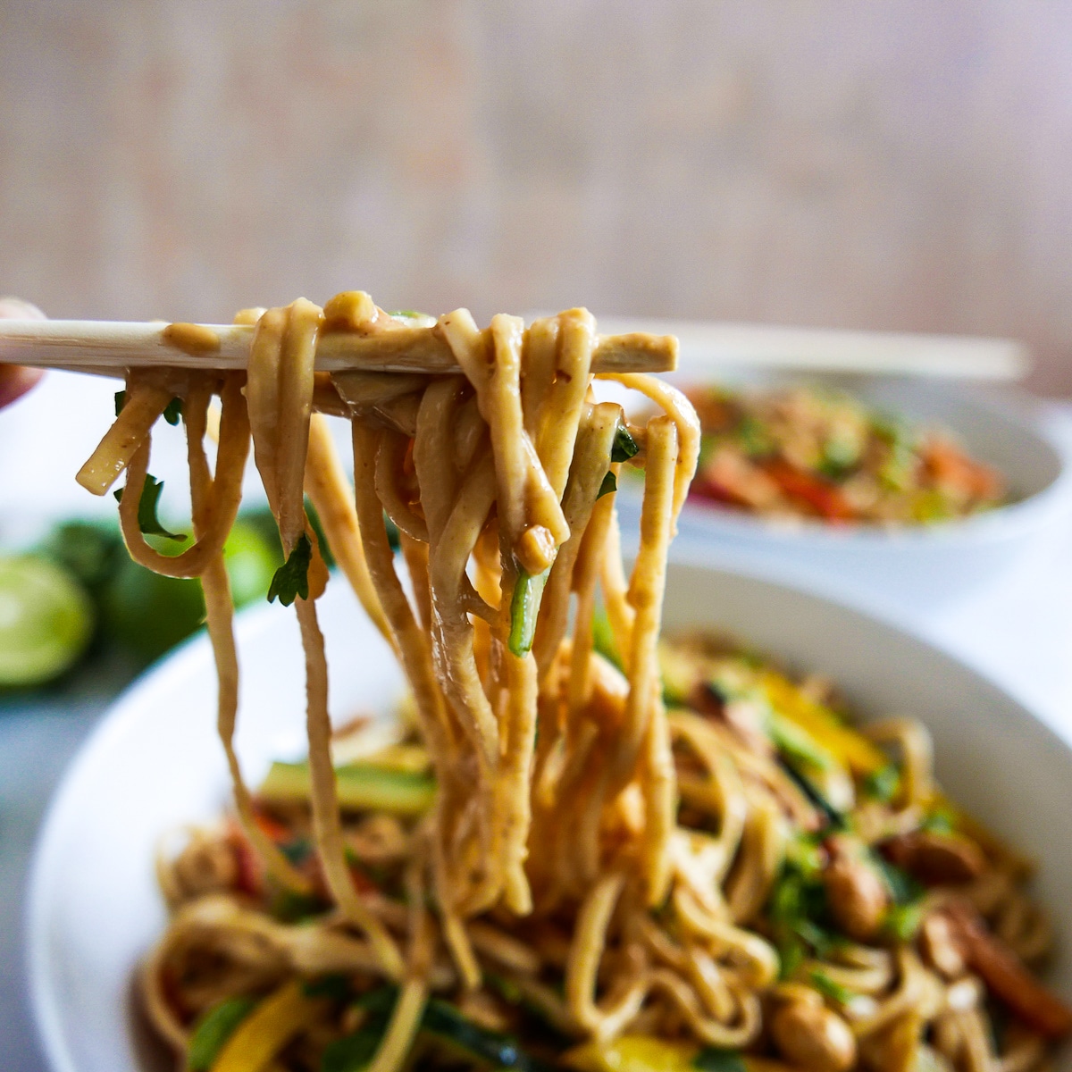 Chopsticks holding up spicy peanut noodles from bowl.