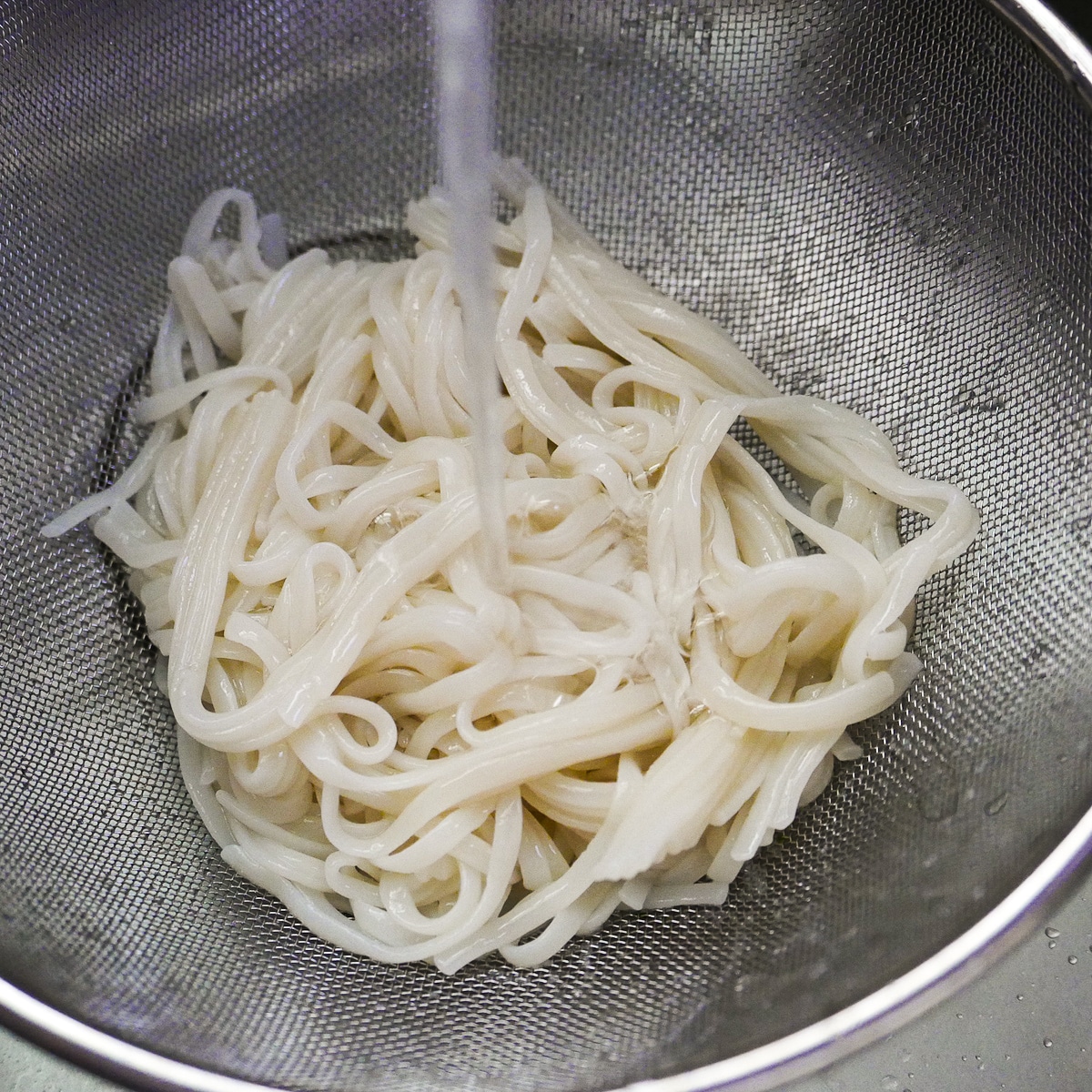 rinsing-noodles.jpg Colander with cooked rice noodles being rinsed under cold water.