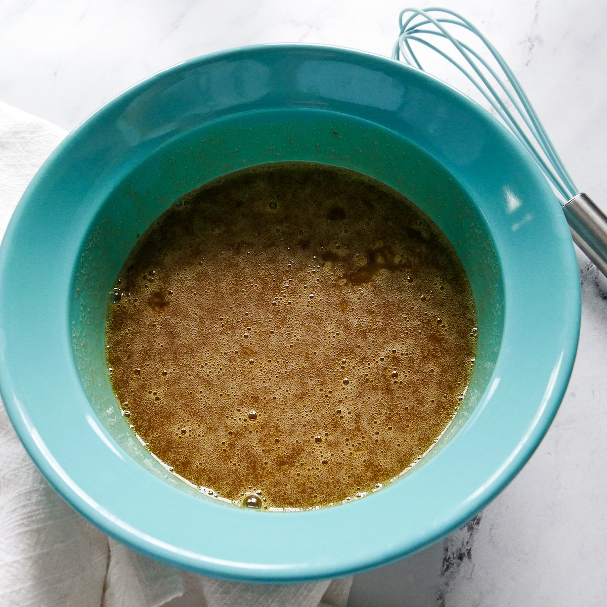 Eggs, oil, brown sugar, and vanilla extract whisked together in a blue bowl.