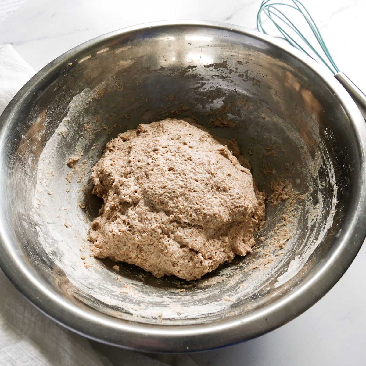 sticky naan dough combined in a bowl with a whisk in the background.