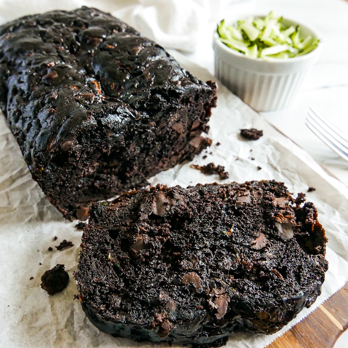 Chocolate zucchini bread with one slice cut on a wooden board lined with parchment paper.