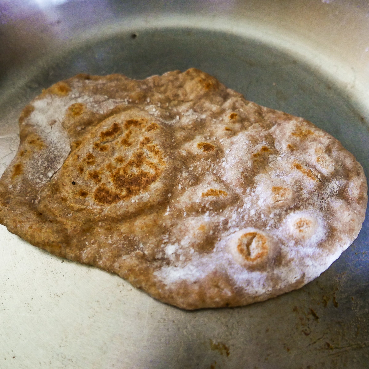 Sourdough naan being cooked in a large skillet.