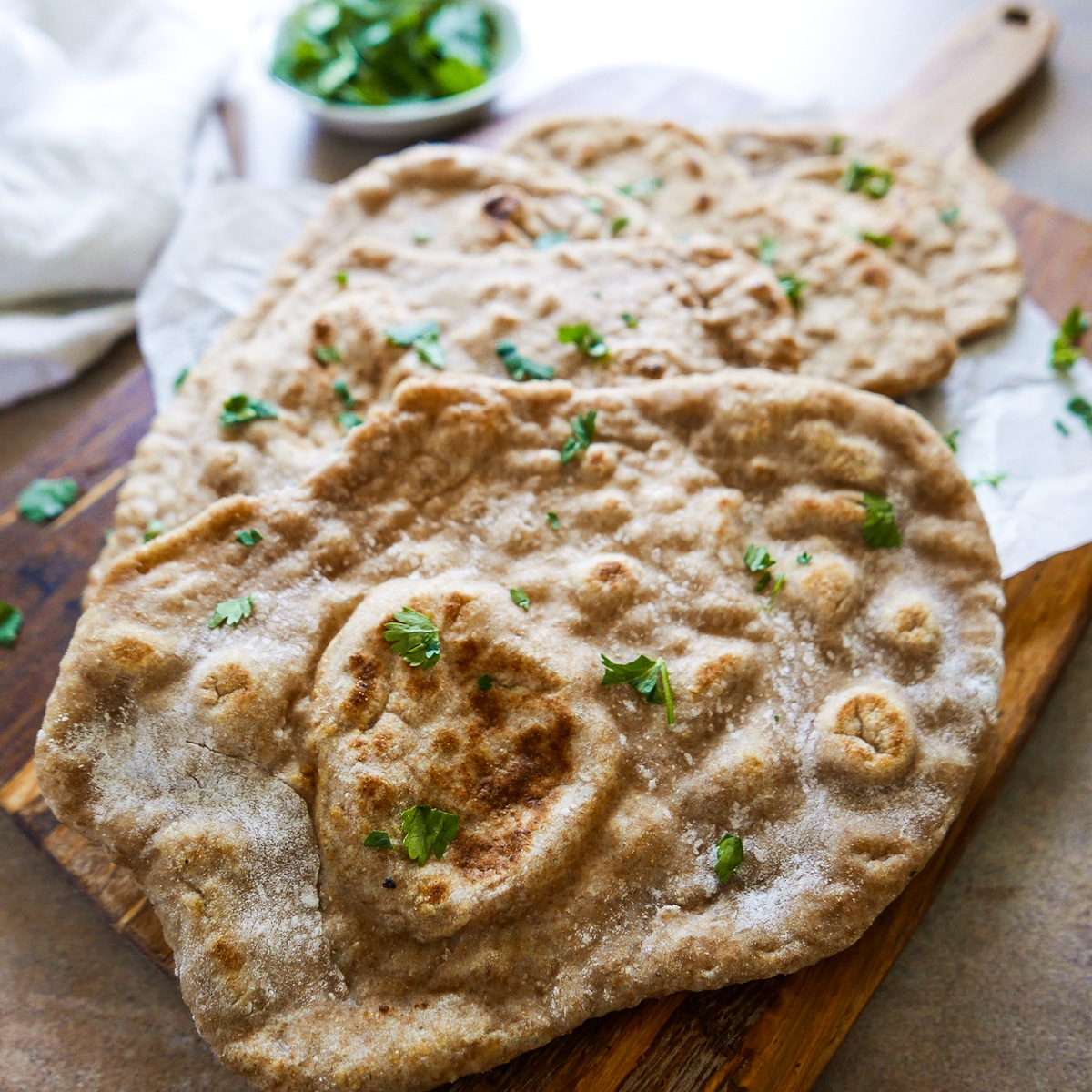 Five pieces of golden brown naan arranged on a wooden board and garnished with chopped cilantro.