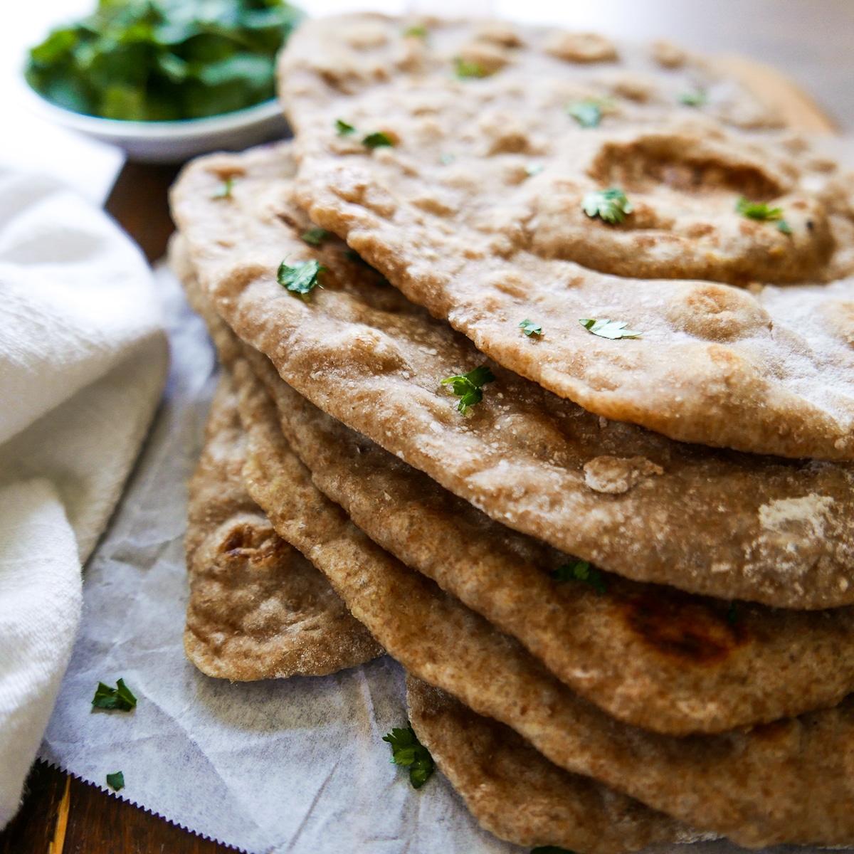 five pieces of naan garnished with cilantro and stacked on a piece of parchment paper.