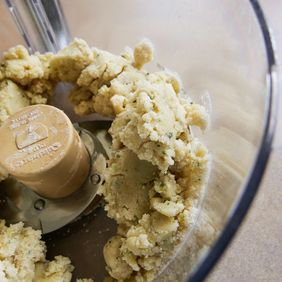 Cookie dough formed into moist clumps in a food processor.