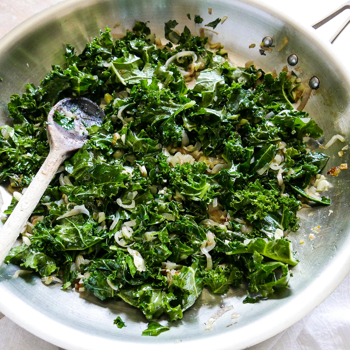 Swiss chard and garlic cooking with caramelized onions in a large skillet.