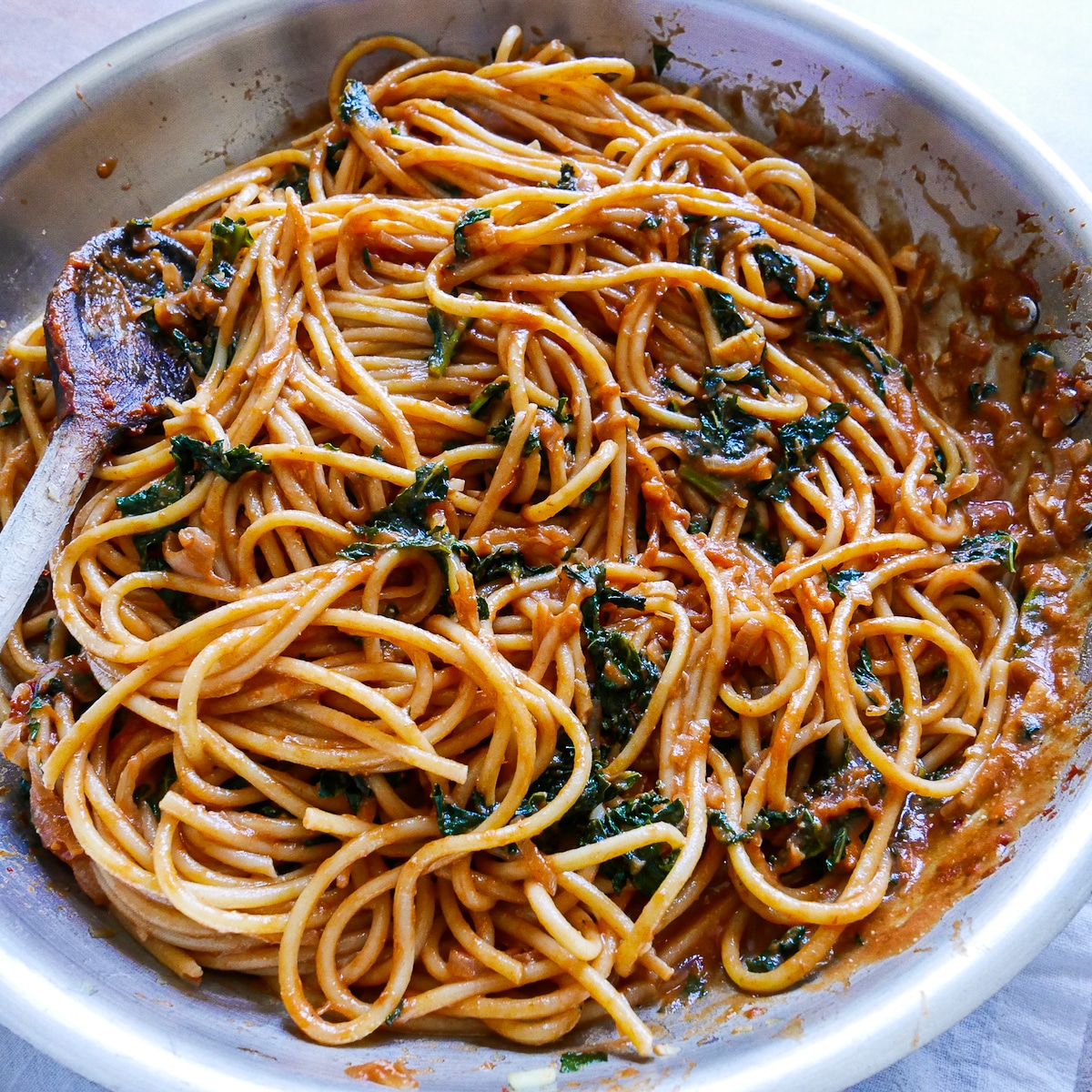 Pasta and pasta water mixed into shallot and Swiss chard mixture with a wooden spoon.