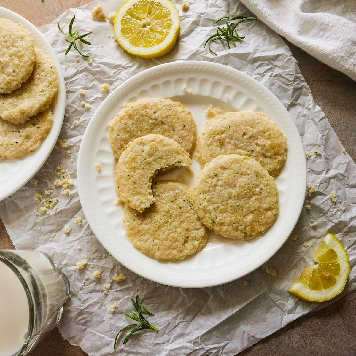Plate of shortbread cookies surrounded by cookie crumbs, lemon slices, and rosemary sprigs. 