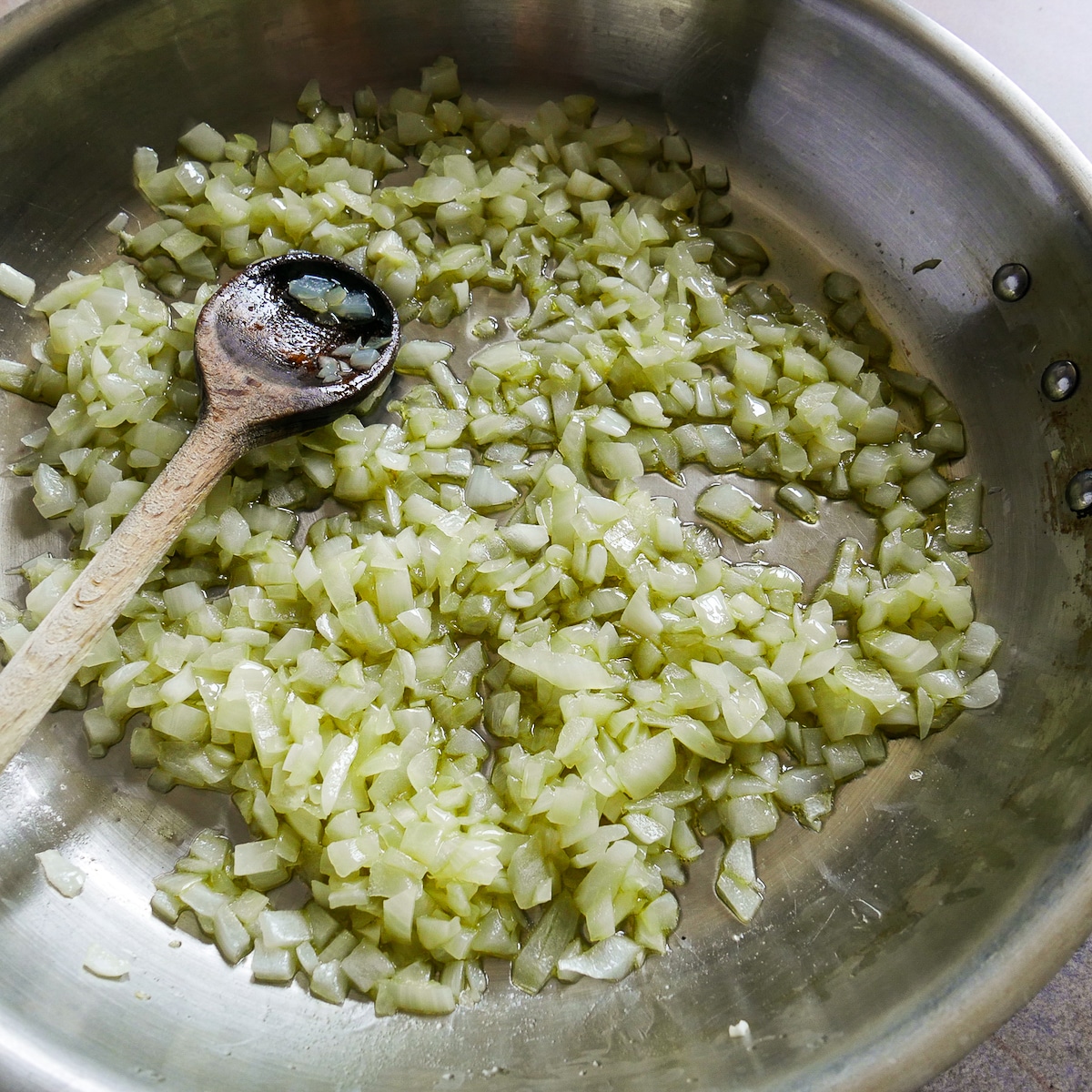 Onions being sauteed in a skillet with a wooden spoon.