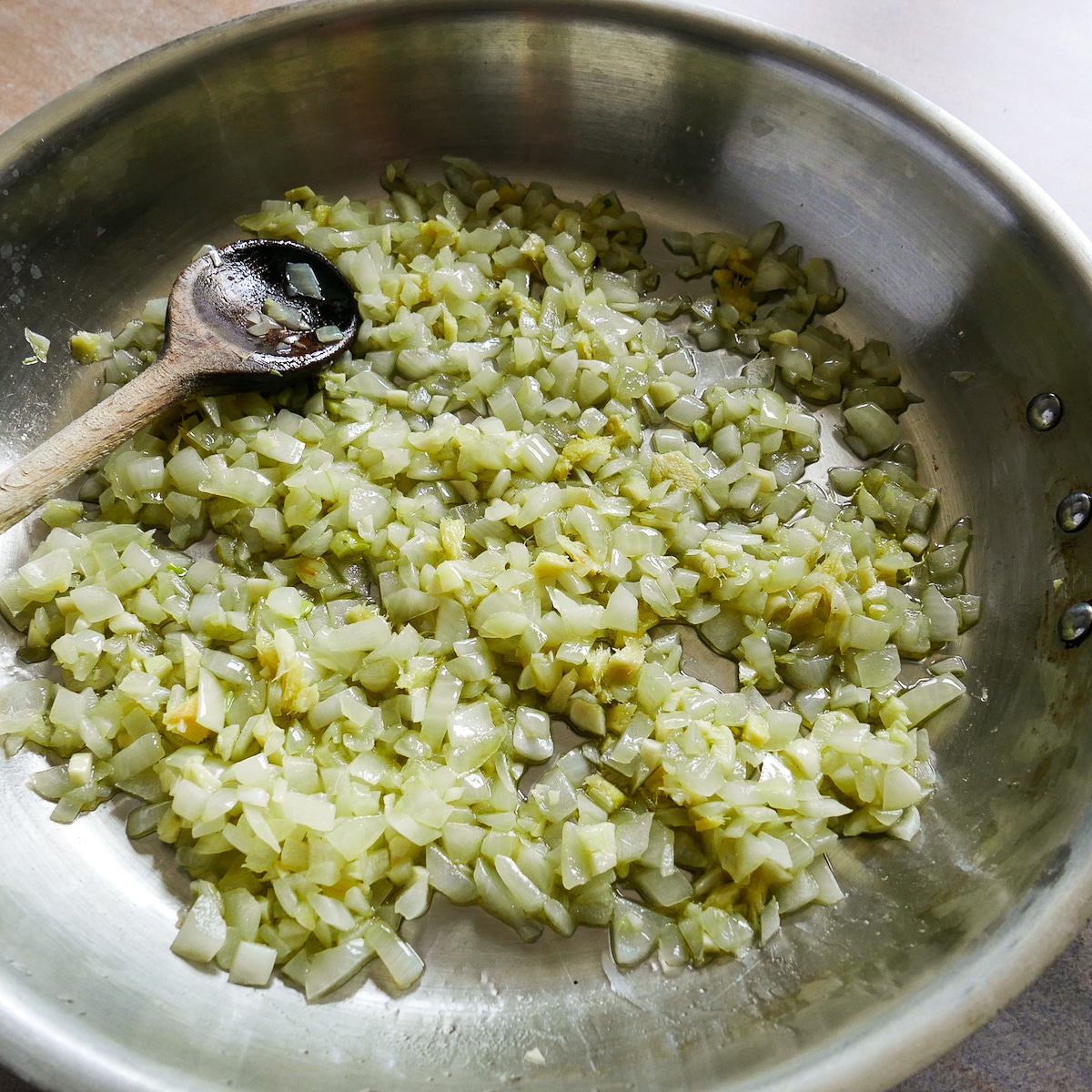 Garlic and ginger being cooked with onions in a large skillet.