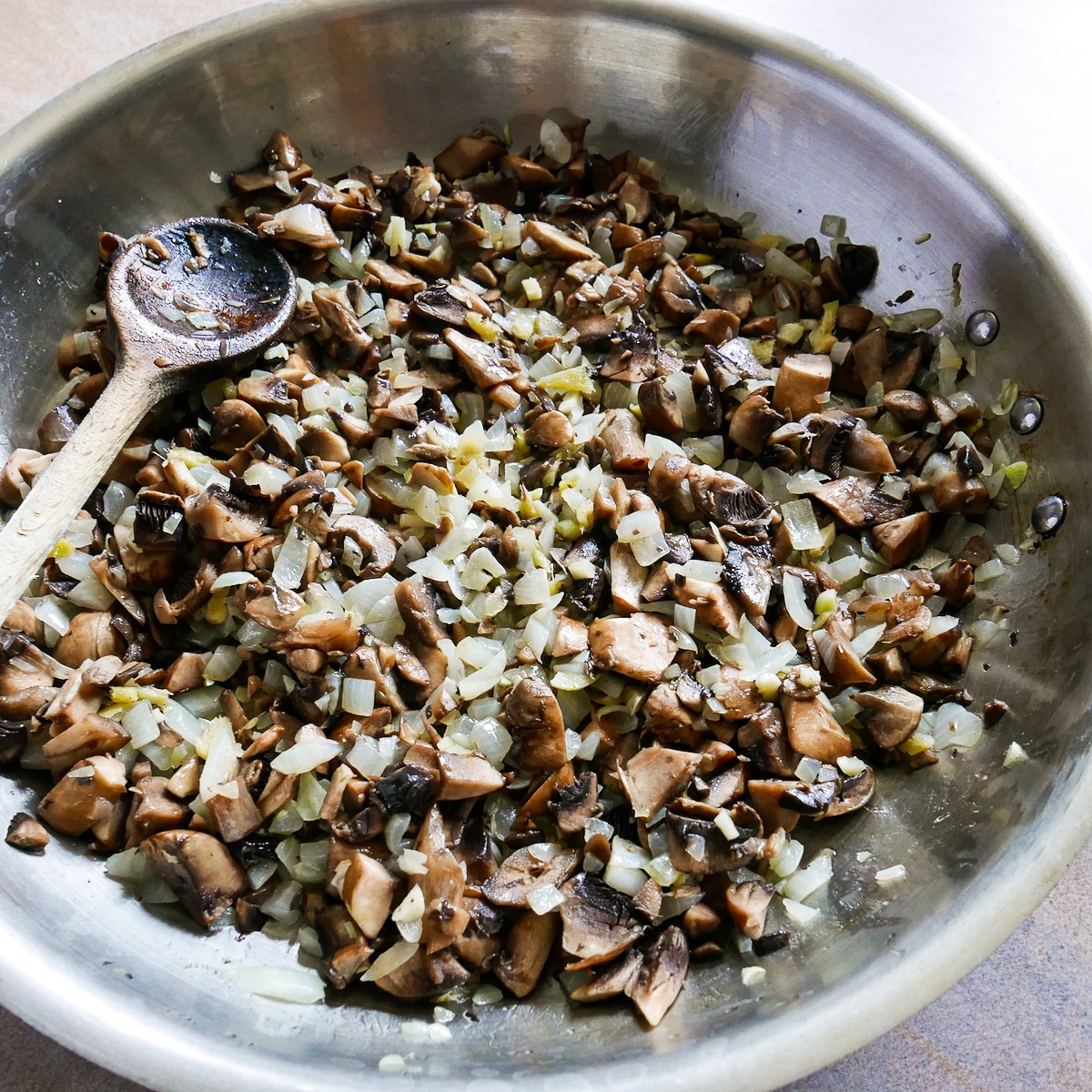 Mushrooms added to onion mixture in a skillet with a wooden spoon.