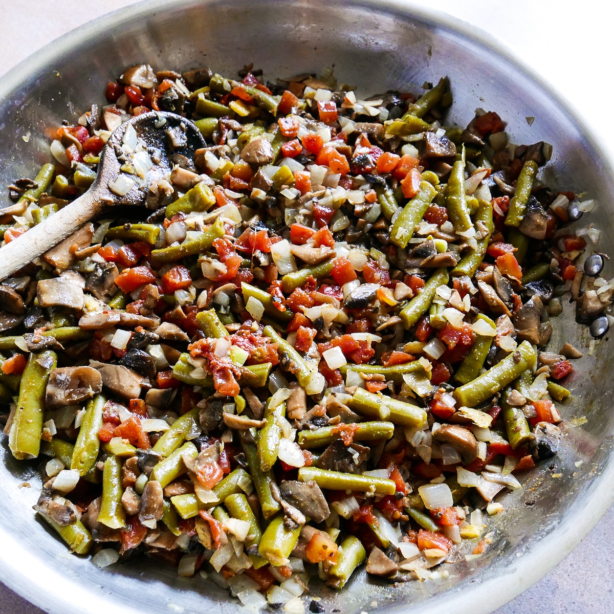 Green beans, tomato, and spices added to mushroom mixture cooking in a large skillet.