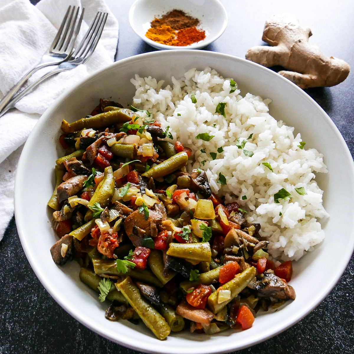 Curry in a white bowl with white rice and ginger and spices in the background.