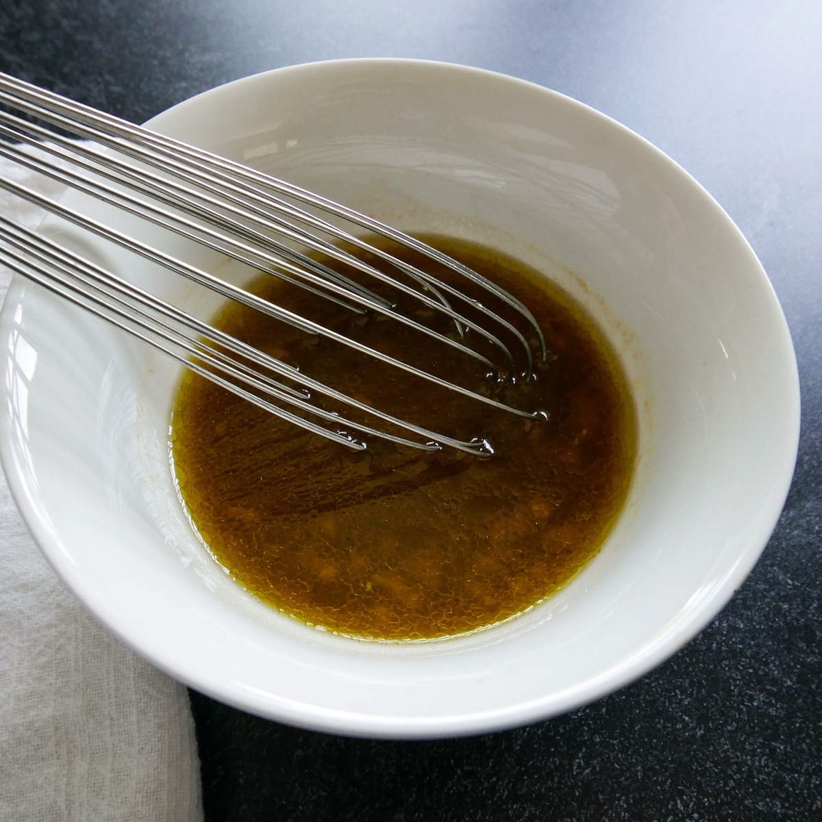 mustard-vinaigrette-being-whisked.jpg mustard vinaigrette being whisked together in a small white bowl.