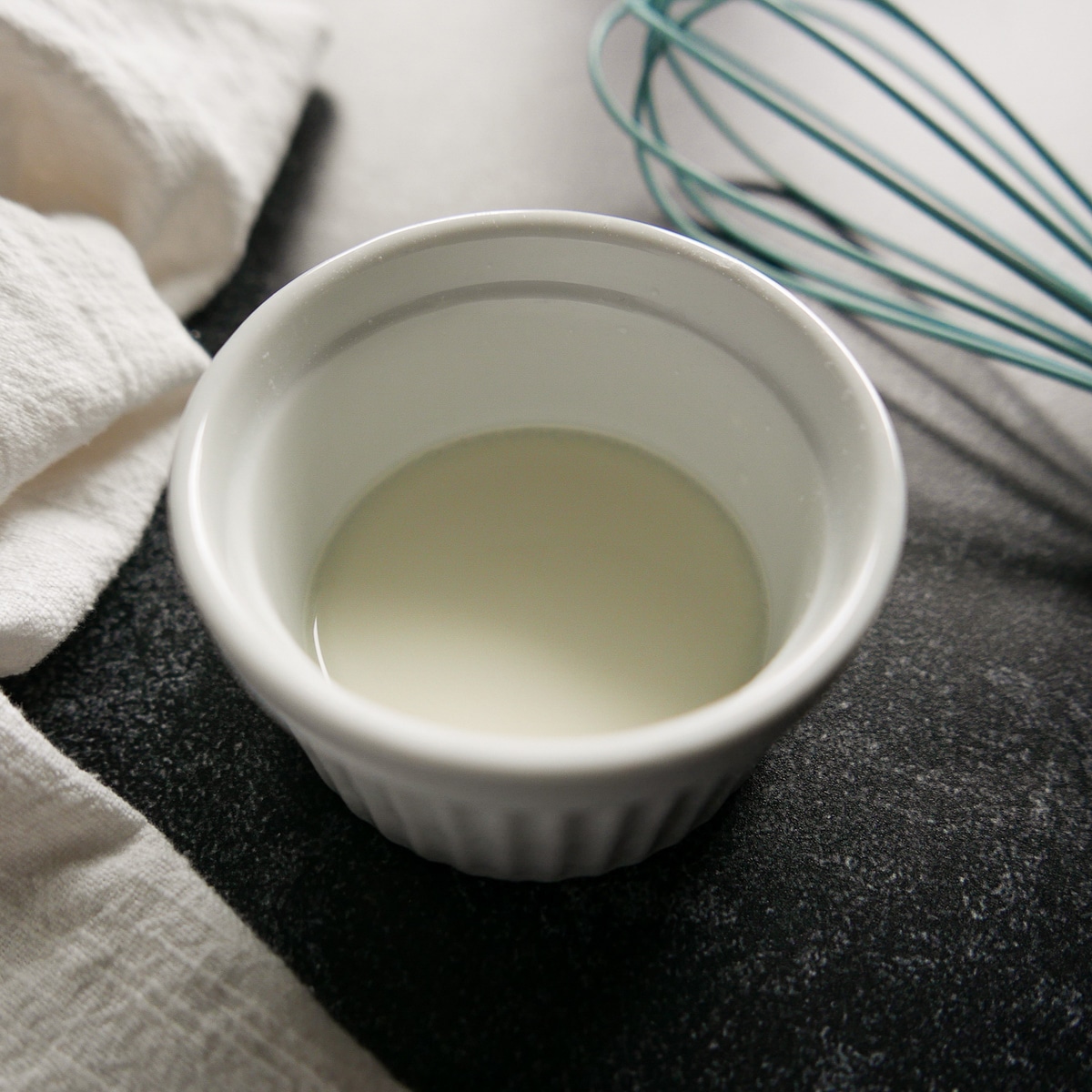 cornstarch-slurry.jpg Cornstarch slurry in a small white bowl with a whisk in the background.