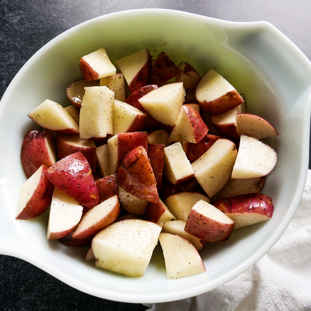 Sliced red potatoes tossed in olive oil in a mixing bowl.