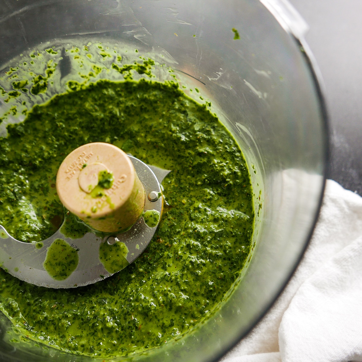 Cilantro chimichurri pureed in a food processor with a napkin next to it. 