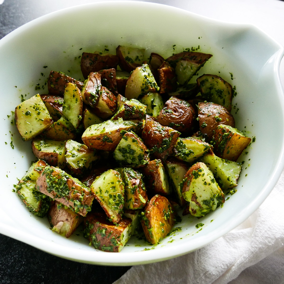 Roasted potatoes tossed with sauce in a mixing bowl.