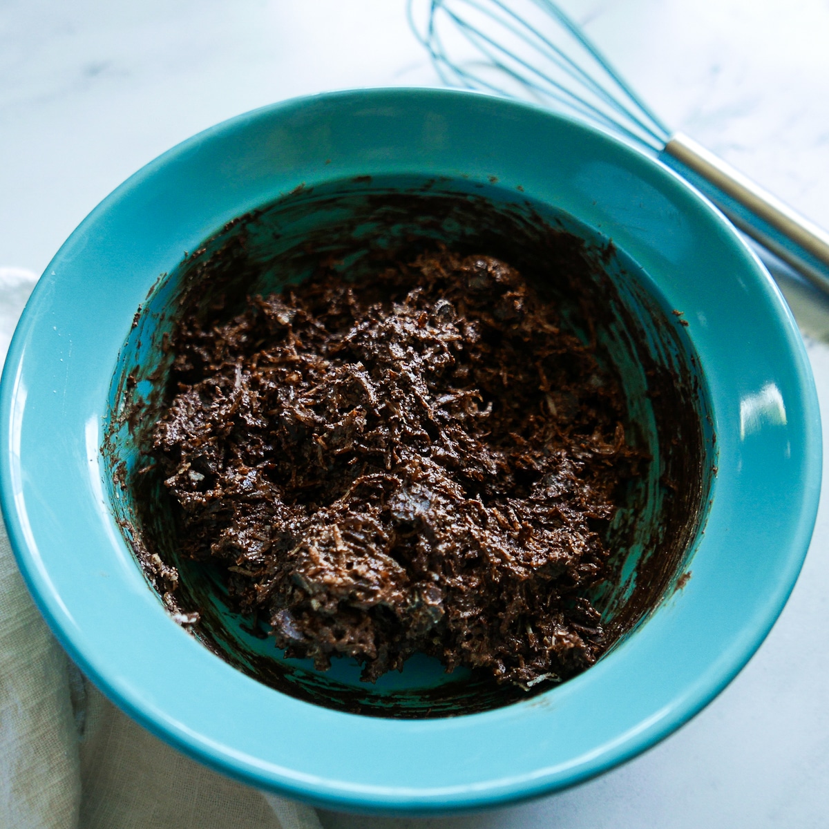 Melted chocolate and coconut folded into whipped egg whites in a blue bowl.