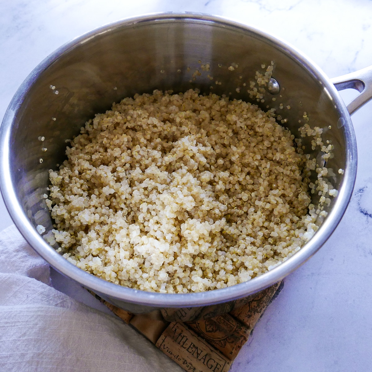 Fluffy quinoa in a saucepan with a white napkin resting nearby.