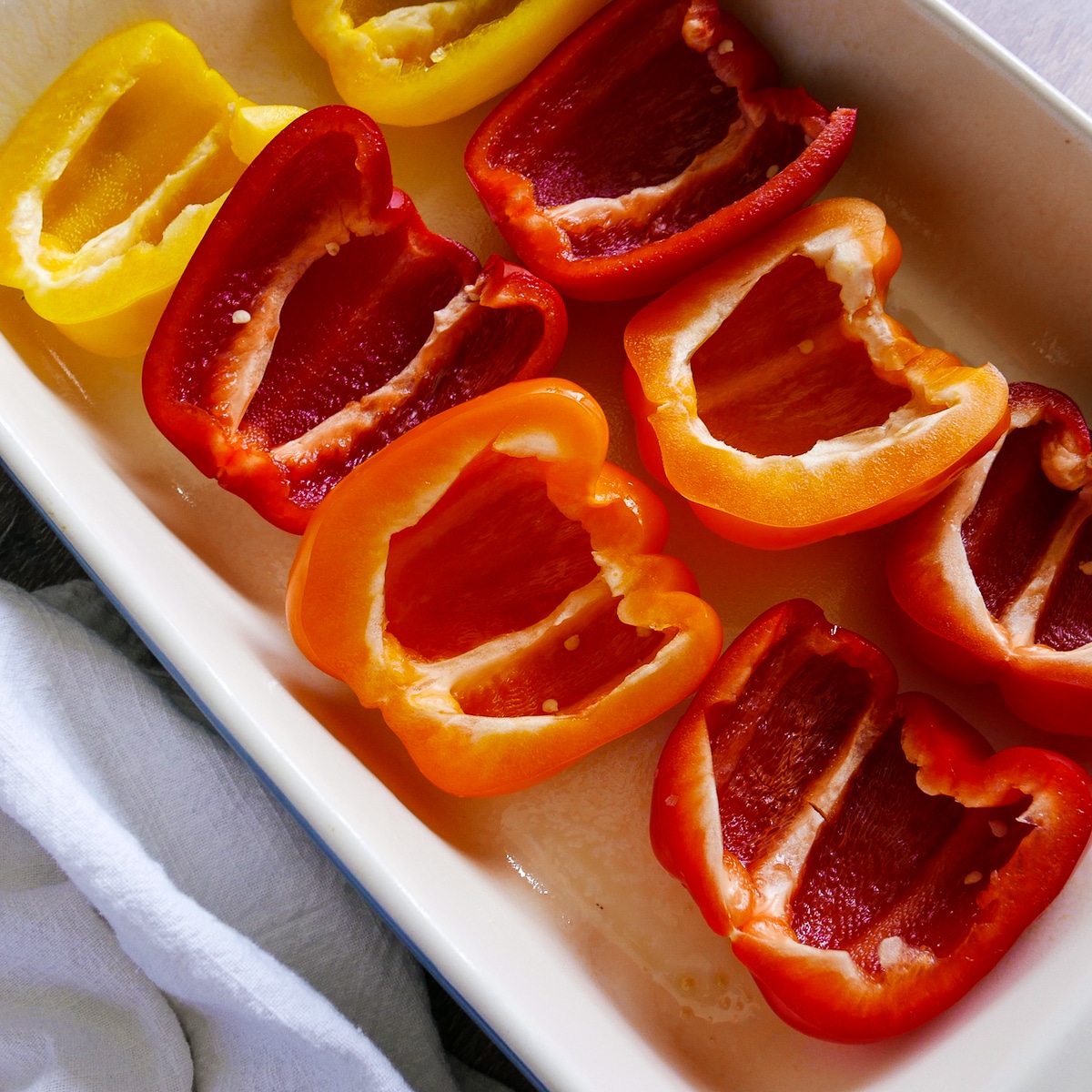 Seeded and halved bell peppers placed cut side up in a baking dish.