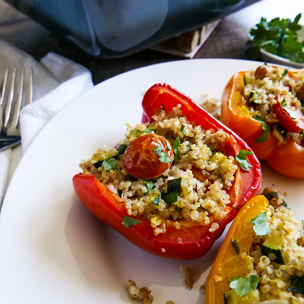 quinoa stuffed peppers on a white plate with forks and fresh parsley in the background. 