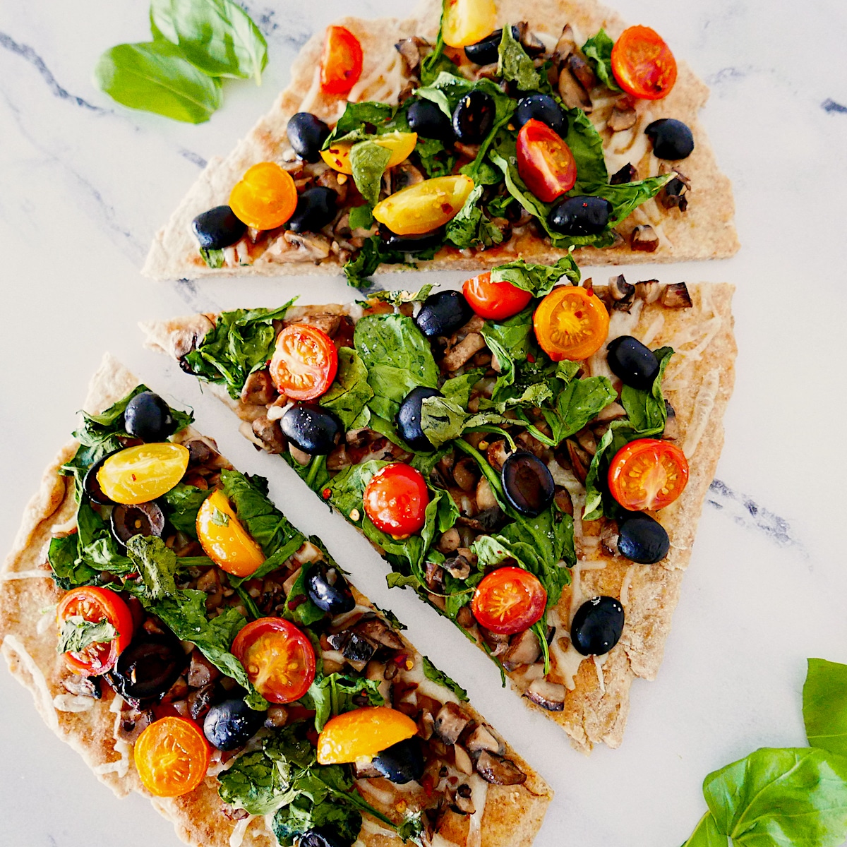 vegan flatbread pizza topped with basil and cut into three slices.
